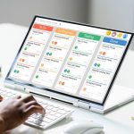 Closeup of hands typing on a computer at a desk in an office with a digital scheduling calendar onscreen.