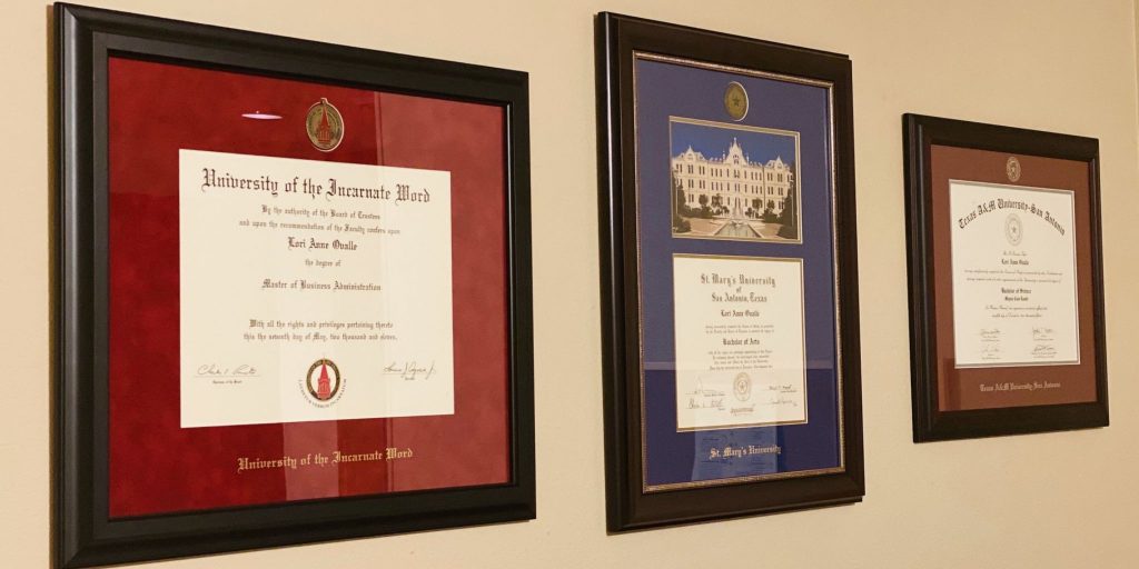 Closeup of the University of the Incarnate Word, St. Mary's University, and Texas A&M San Antonio diploma frames on wall.