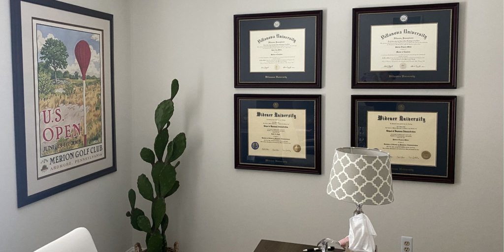 Office with two Villanova University and two Widener University diploma frames on wall next to cactus and framed poster.