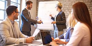 Two people leading meeting and holding markers as they write ideas on large paper pad.