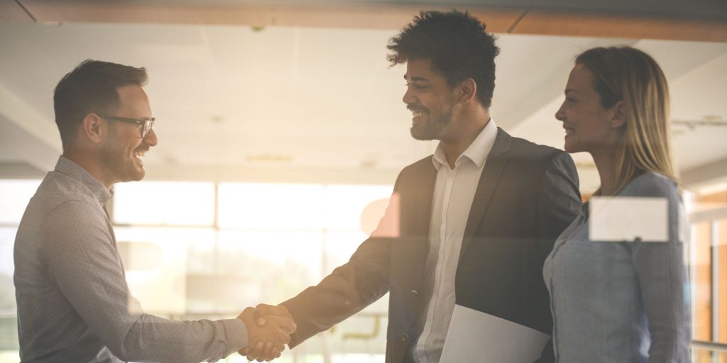 People shaking hands in brightly lit office with sun shining through windows behind them.