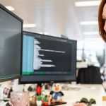 Closeup of a woman at desk working on computer with several screens surrounding her.