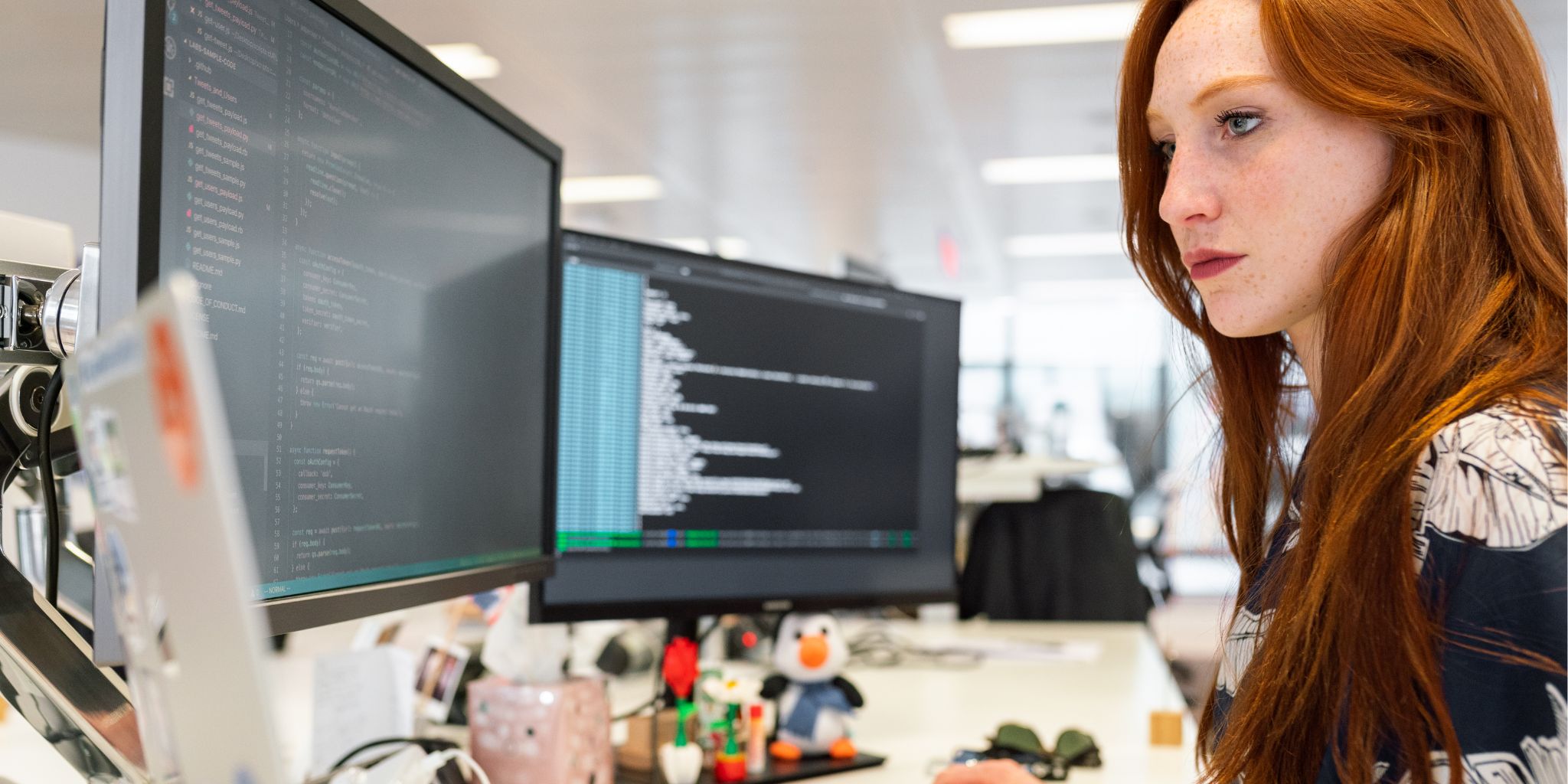 Closeup of a woman at desk working on computer with several screens surrounding her.