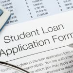 Closeup of hand with pen filling out a Student Loan Application Form with calculator nearby.