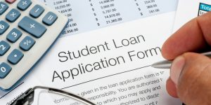 Closeup of hand with pen filling out a Student Loan Application Form with calculator nearby.