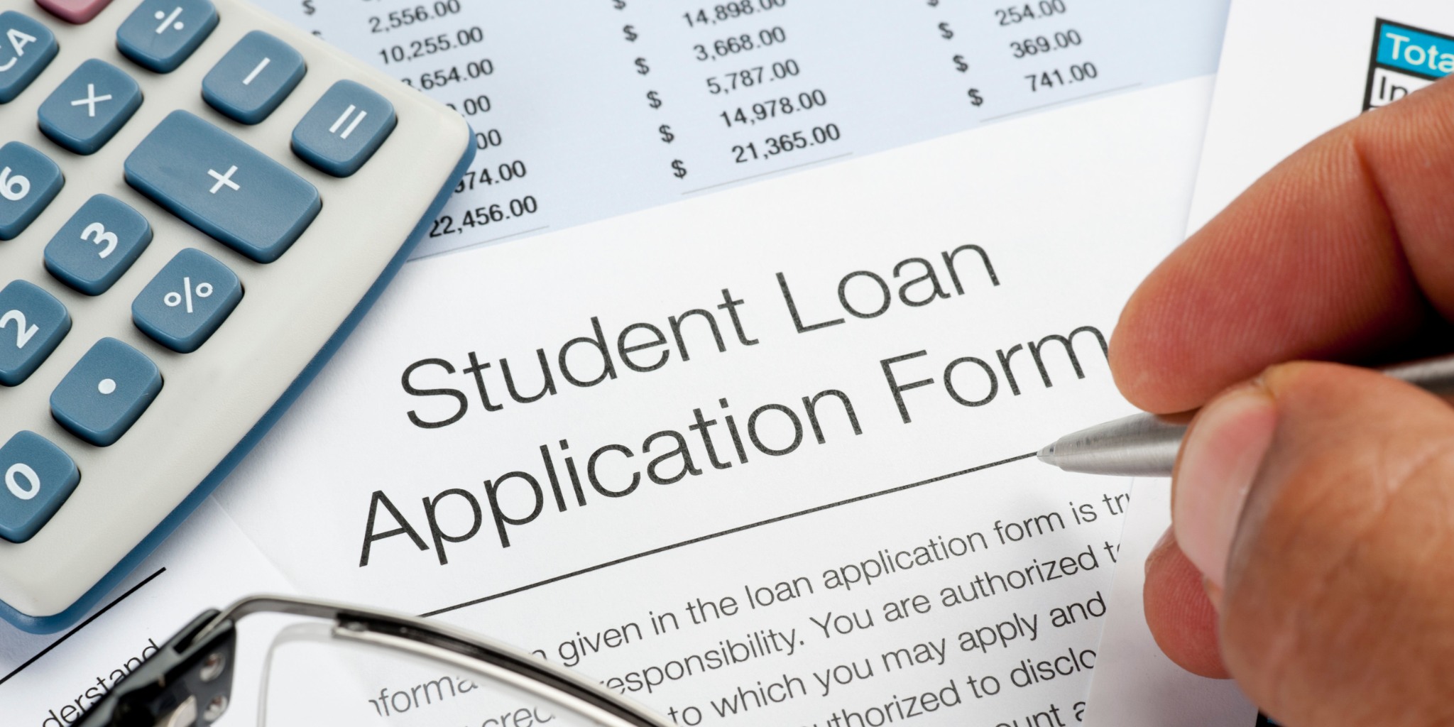 Closeup of hand with pen filling out a Student Loan Application Form with calculator nearby.
