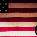 A military officer facing lifesize American flag and saluting it.