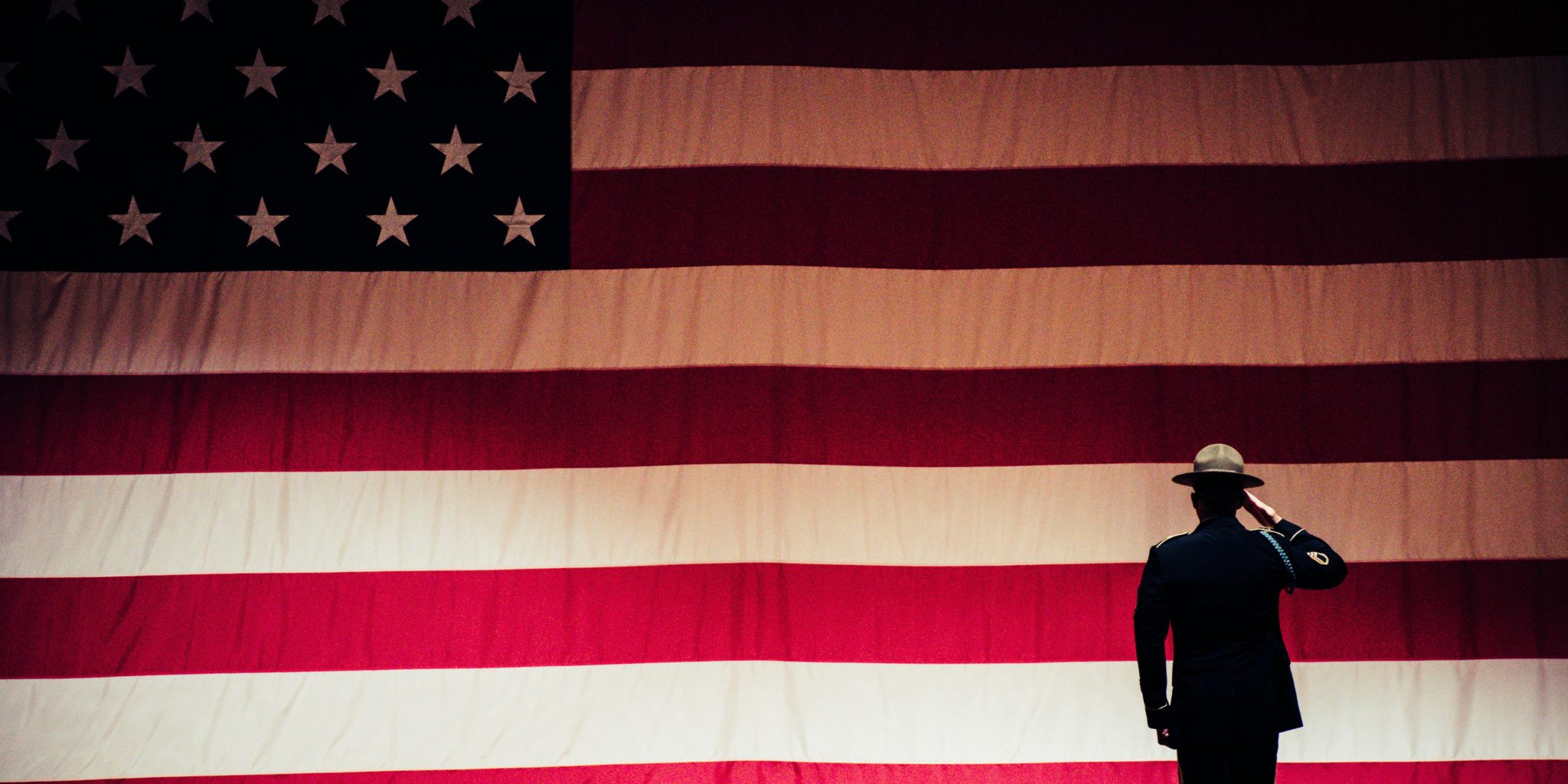 A military officer facing lifesize American flag and saluting it.