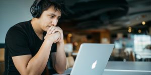 Man with headphones leaning his chin on clasped hands in cafe working on lap