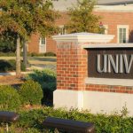 Campus photo of brick buildings and a sign that reads University.
