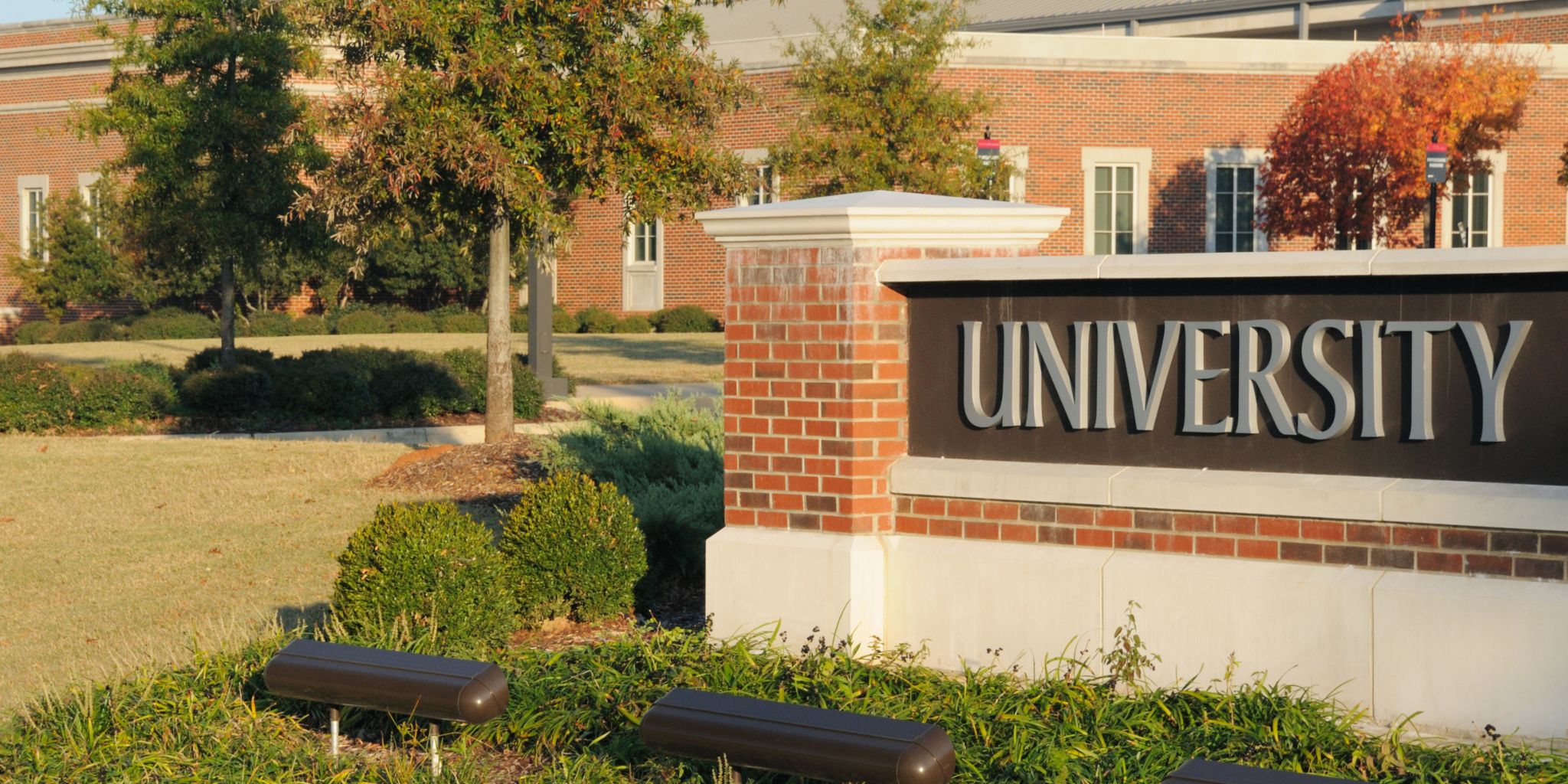 Campus photo of brick buildings and a sign that reads University.