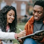 Students sitting on lawn campus with notebooks and pens working together on homework.
