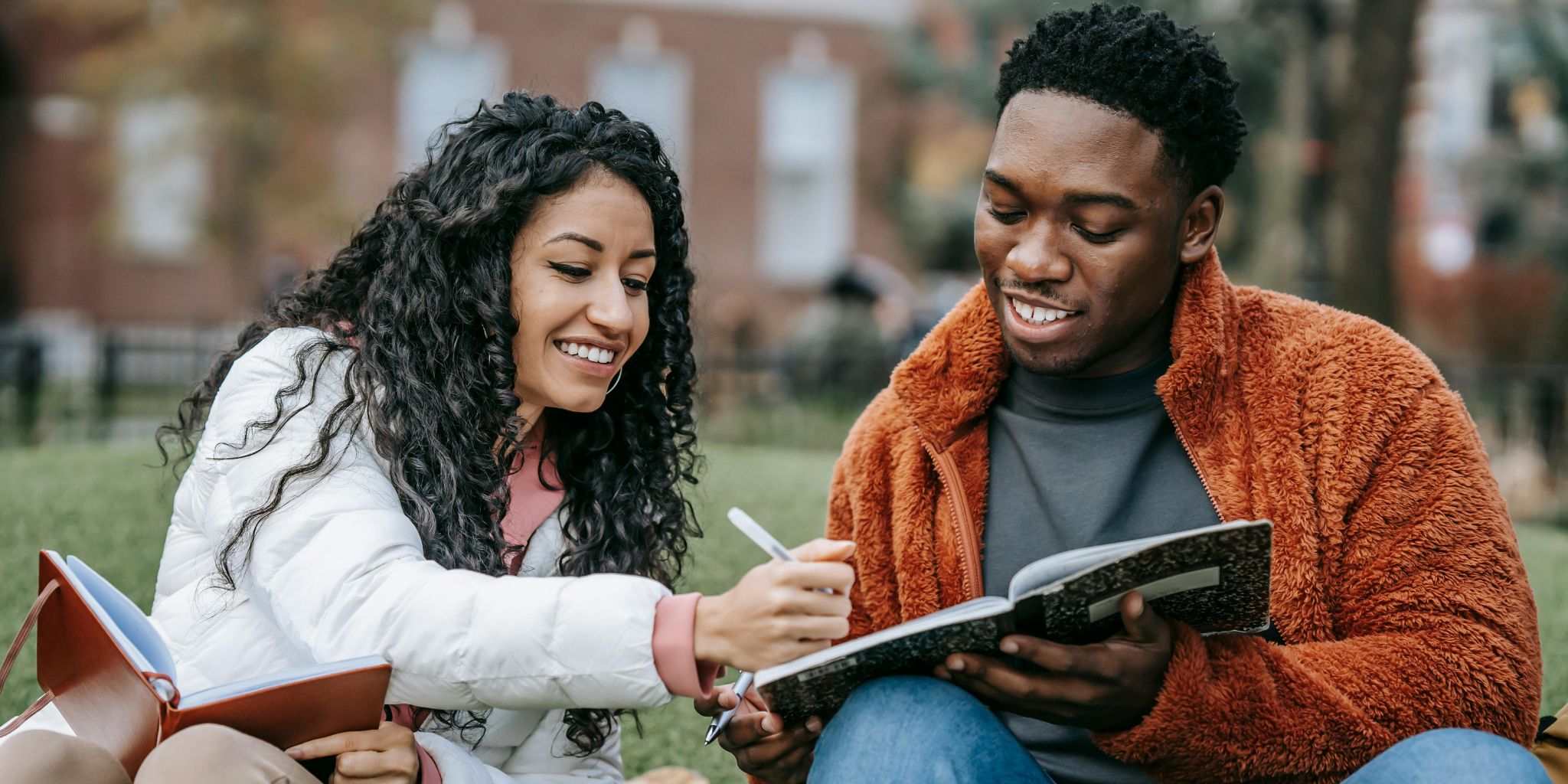 Students sitting on lawn campus with notebooks and pens working together on homework.