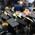 A sea of black grad caps, some with designs on them, during a commencement ceremony.