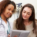 Nurse with stethoscope showing chart to patient in white medical office.