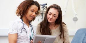 Nurse with stethoscope showing chart to patient in white medical office.