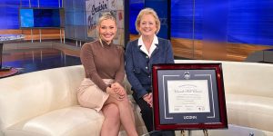 CEO Lucie Voves smiling with news anchor and custom UCONN diploma frame