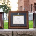 Three Simsbury State University diploma frames showcased on stone wall on college campus.