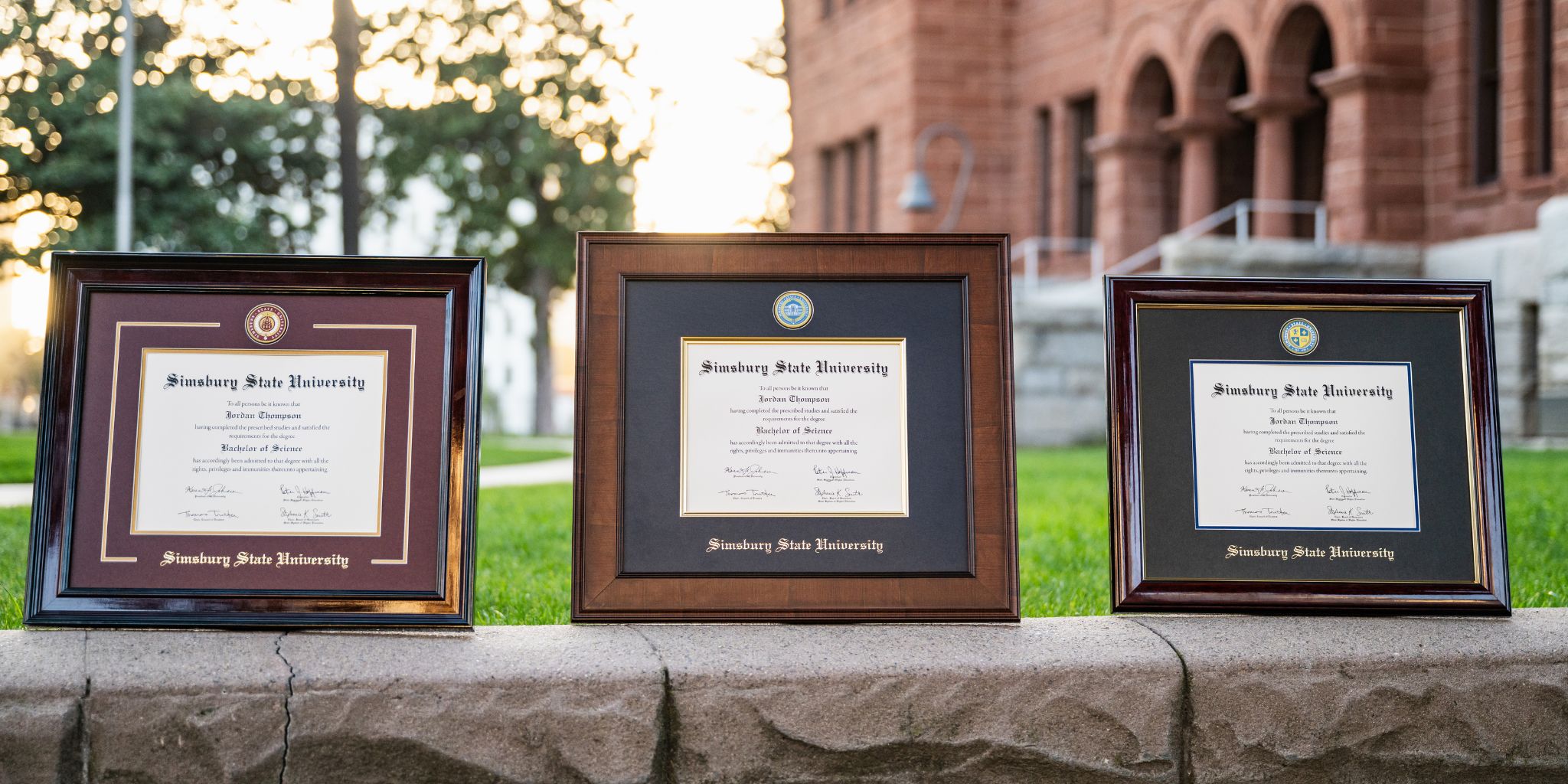 Three Simsbury State University diploma frames showcased on stone wall on college campus.