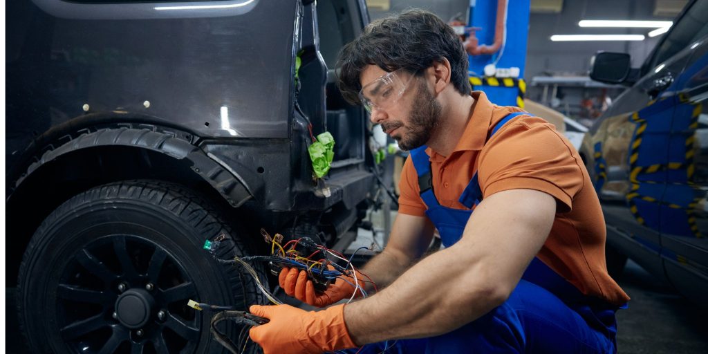 Mechanic wearing gloves and goggles working on a car.