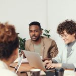 Coworkers in a conference room working and talking while on laptops.