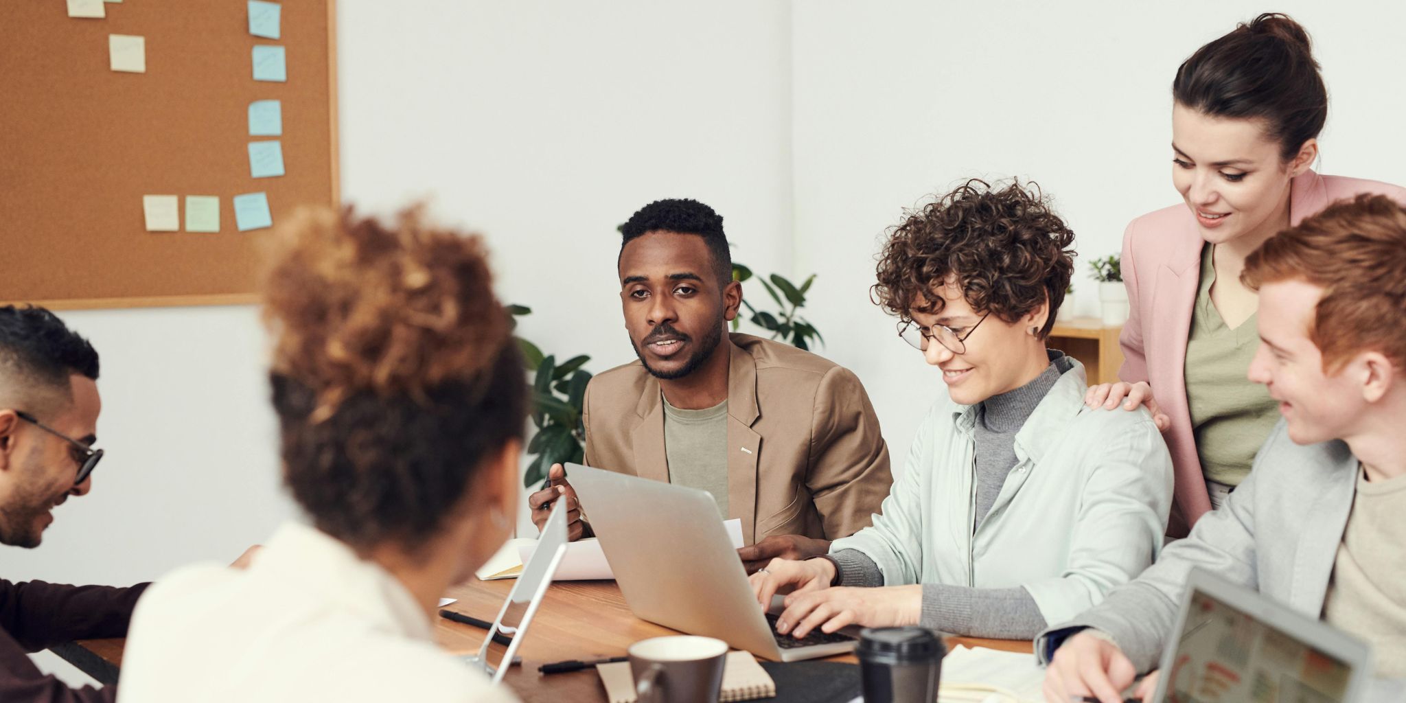 Coworkers in a conference room working and talking while on laptops.