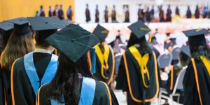 The backs of master's graduates wearing doctoral sashes and hoods as they proceed toward the graduation stage.