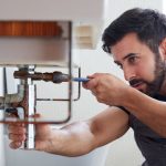 Plumber using wrench to turn pipes under sink area.