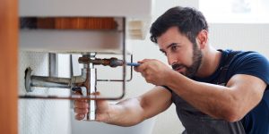 Plumber using wrench to turn pipes under sink area.