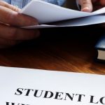 Closeup of hands going through papers at desk with books and a paper that says Student Loan on it.