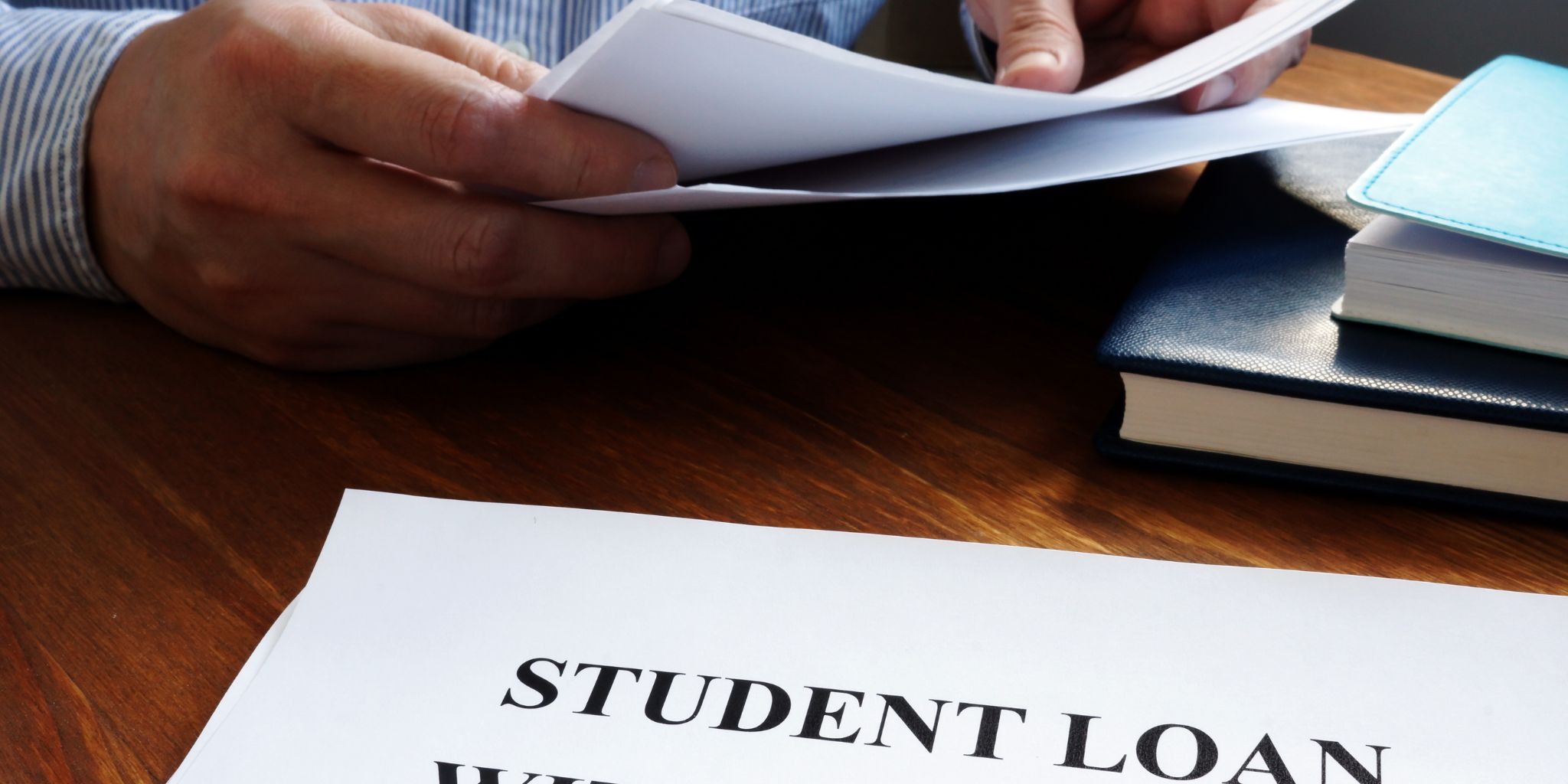 Closeup of hands going through papers at desk with books and a paper that says Student Loan on it.