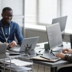 Three IT workers working on their laptops in an office at a communal table.