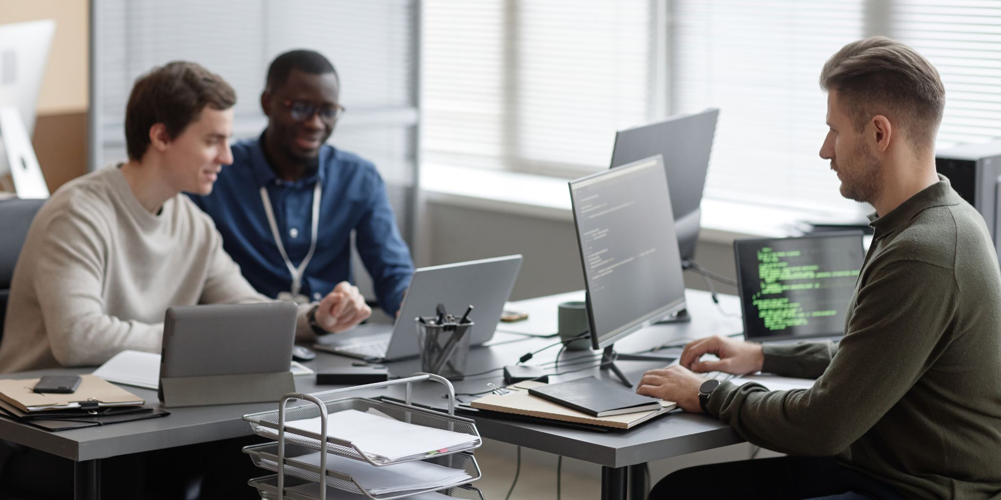 Three IT workers working on their laptops in an office at a communal table.