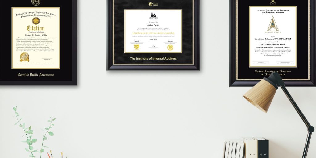 Office wall with CPA certificate frame, Institute of Internal Auditors certificate frame, and NAIFA certificate frame with desk lamp and books in photo.