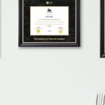 Office wall with CPA certificate frame, Institute of Internal Auditors certificate frame, and NAIFA certificate frame with desk lamp and books in photo.