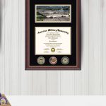 Home office area with Oklahoma State University diploma frame, American Military University diploma frame with challenge coins, and Purple Heart frame over desk with coffee cup and pencil holder.