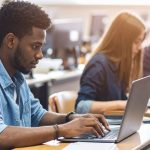 College students in classroom at desks with laptops open and working.