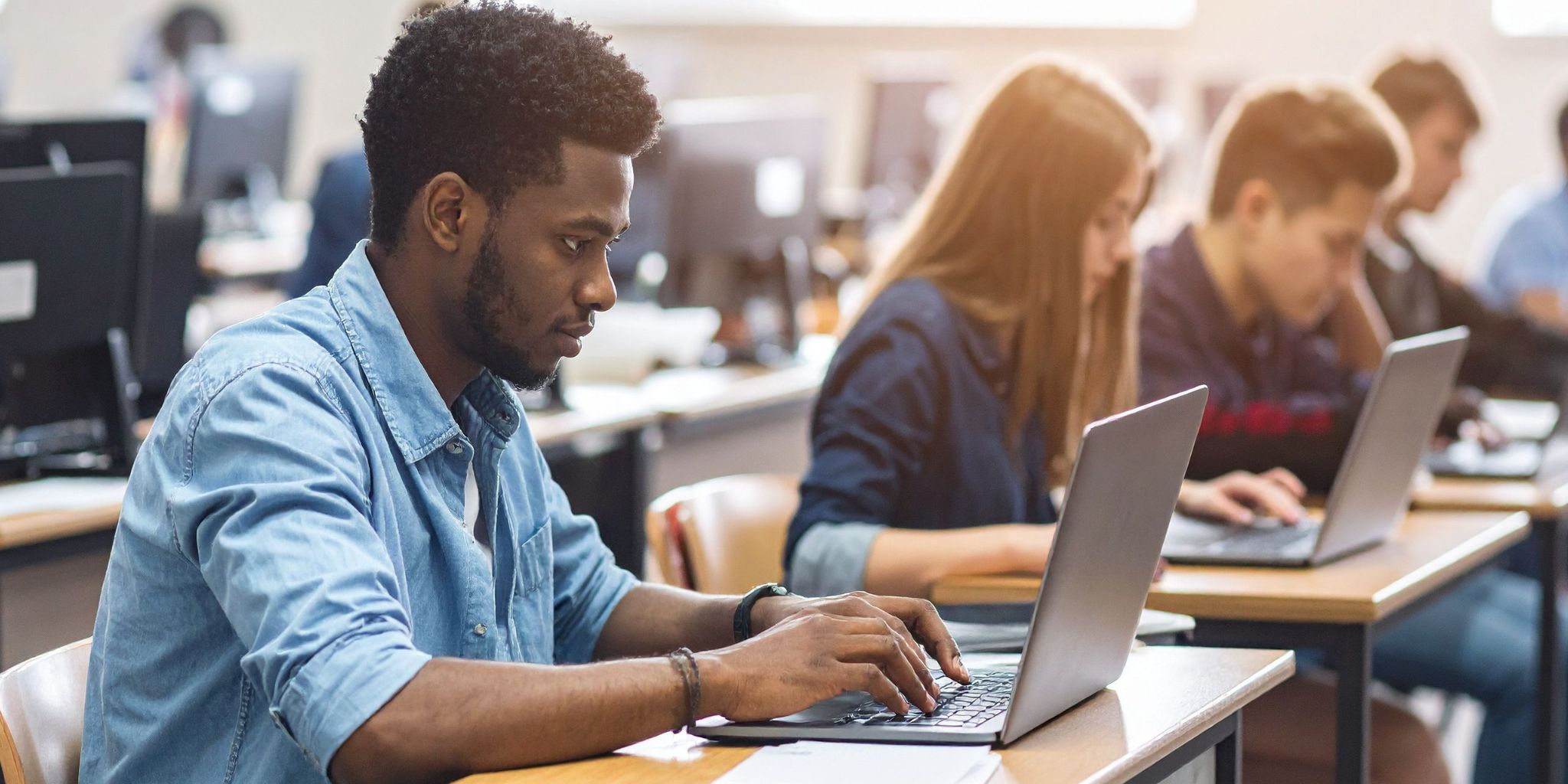College students in classroom at desks with laptops open and working.
