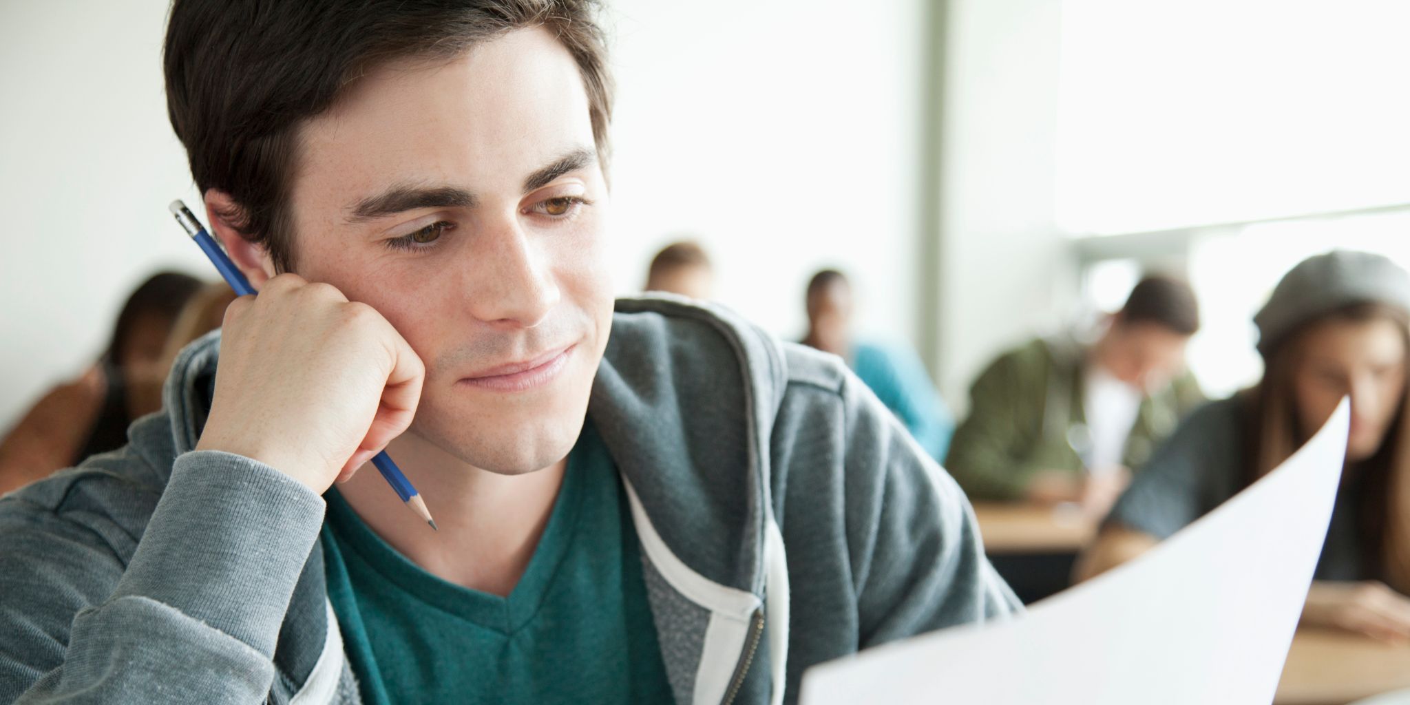 College student sitting in classroom looking at sheet of paper, holding pencil in hand, looking pensive.