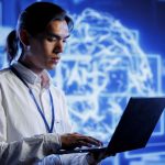 Person holding laptop and wearing lanyard in front of large screen behind them featuring AI tech graphic.