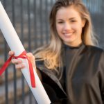Graduate holding a rolled up diploma with a red ribbon around it.