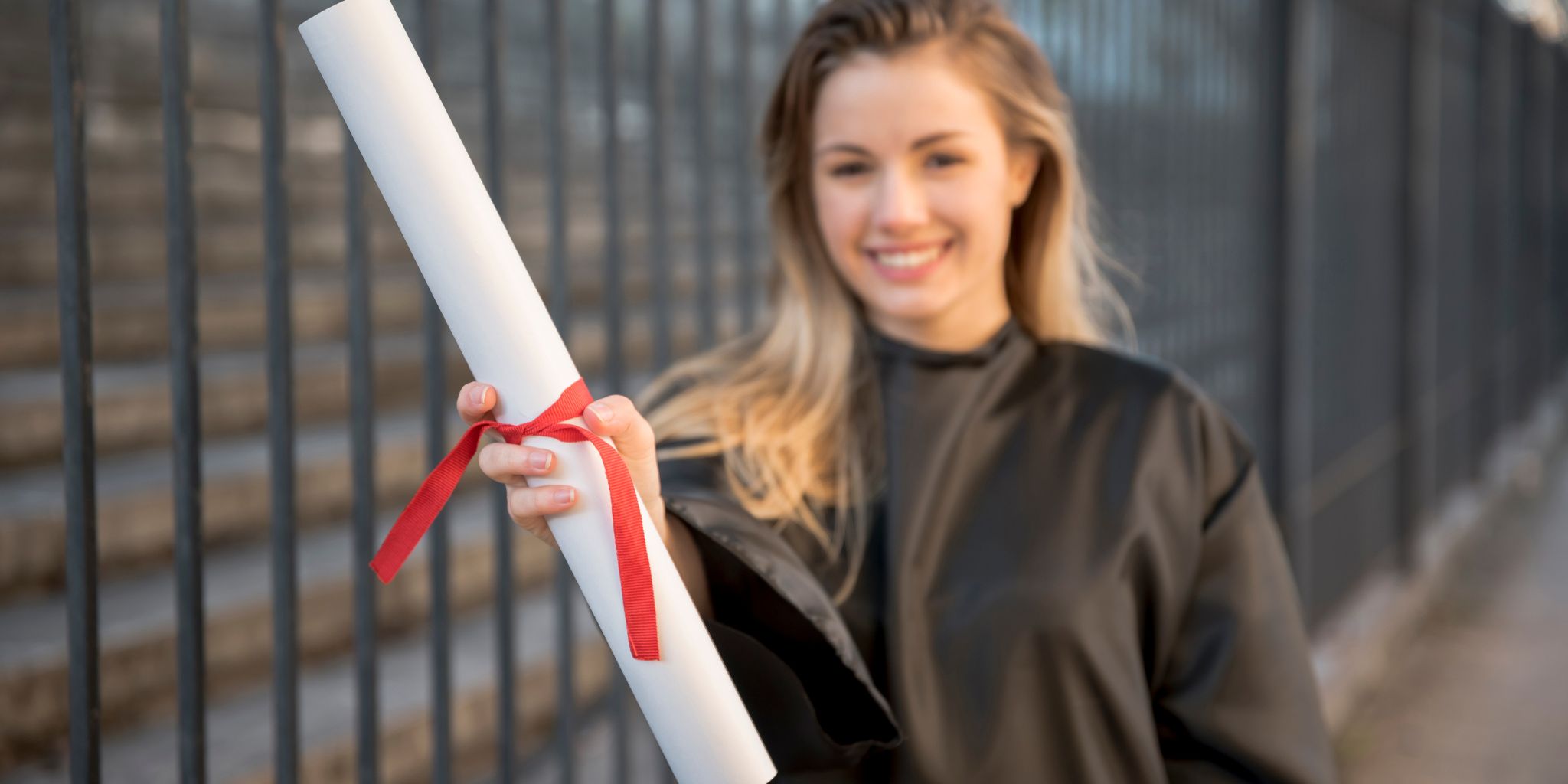 Graduate holding a rolled up diploma with a red ribbon around it.