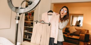 Woman in living room in front of web camera holding business suit on camera and talking about the clothing.