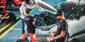People working in an automative garage on a car with hood up.