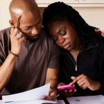 Couple working on papers and looking at a pink calculator together trying to work out expenses.