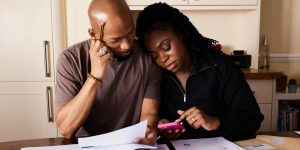 Couple working on papers and looking at a pink calculator together trying to work out expenses.
