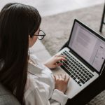 College student sitting on floor of living room working on laptop