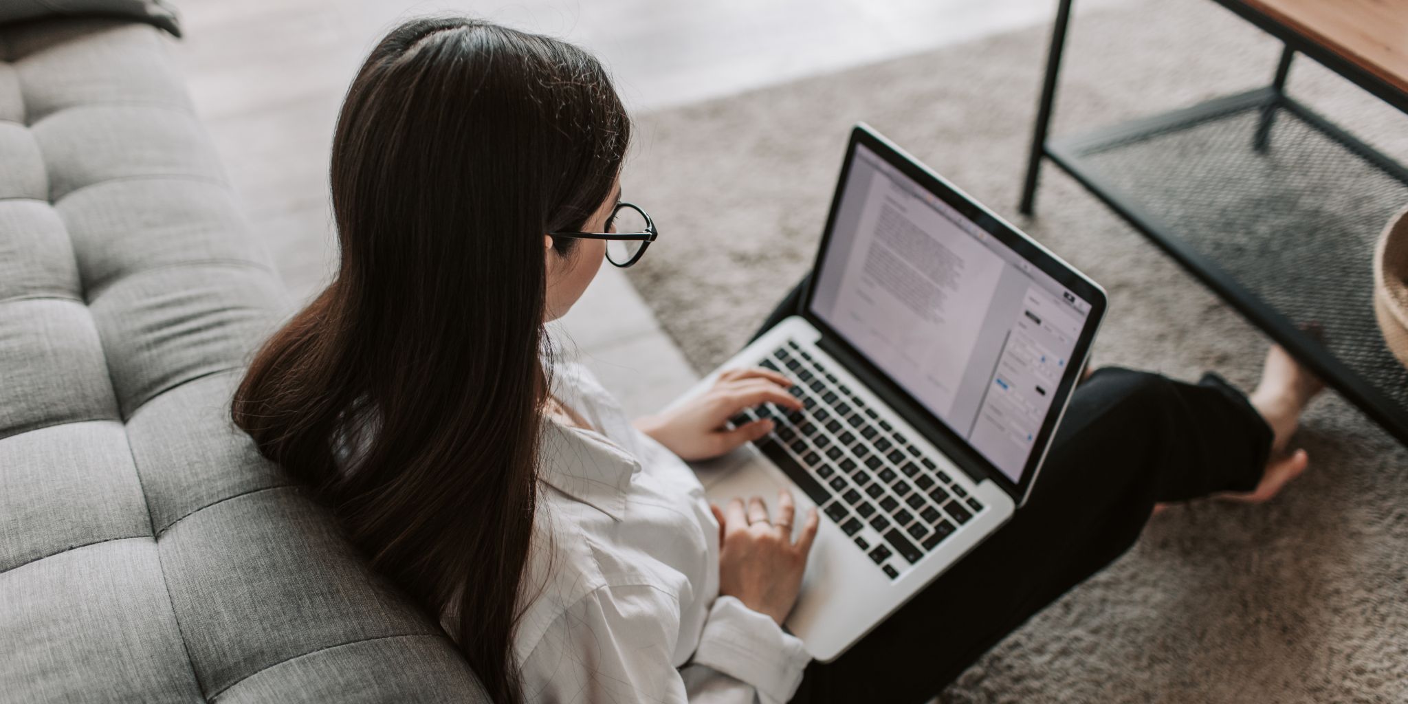College student sitting on floor of living room working on laptop