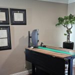 Collection of diploma frames in a home office with a desk, bonsai plant, and a wall sign that says "TS Therapy Services Morgan Hill".