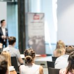 Crowded conference of businesspeople listening to a speaker holding a microphone at a conference